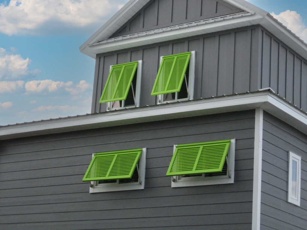 Green hurricane bahama shutters installed on a gray coastal house.